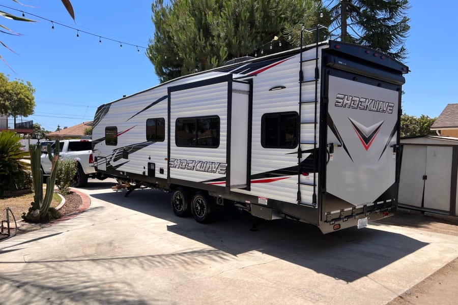 White SHOCKWAVE toy hauler RV rental parked on a sunny driveway. This large travel trailer has black & red accents.