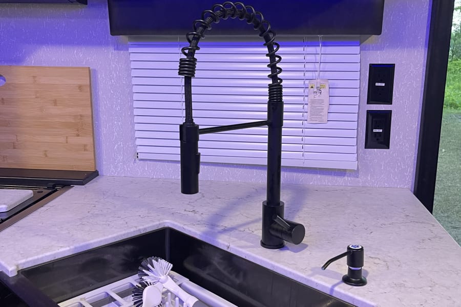 Modern RV rental kitchen with a sleek black sink, industrial faucet, white counters, and blue accent lighting.
