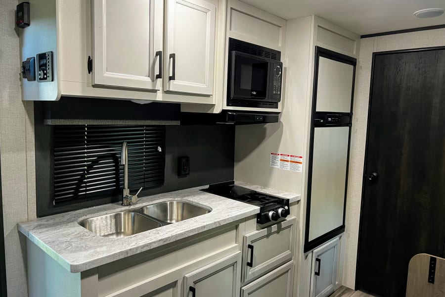 Compact and modern RV rental kitchen with double sink, stove, microwave, and refrigerator, ideal for travel adventures.
