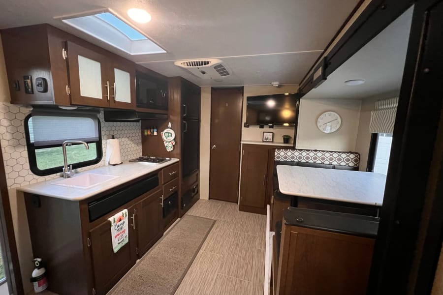 Well-appointed RV rental interior: kitchen with microwave, sink, and cabinets, plus a dinette and TV. Ready for your next trip.