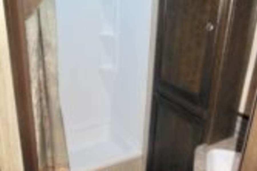 RV rental: Compact RV bathroom with a bright white shower stall and dark wood storage cabinet, offering travel comfort.