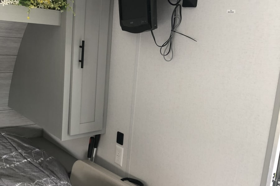 RV rental bedroom featuring a wall-mounted TV, overhead storage cabinet, and bed. Ideal for comfortable travel.