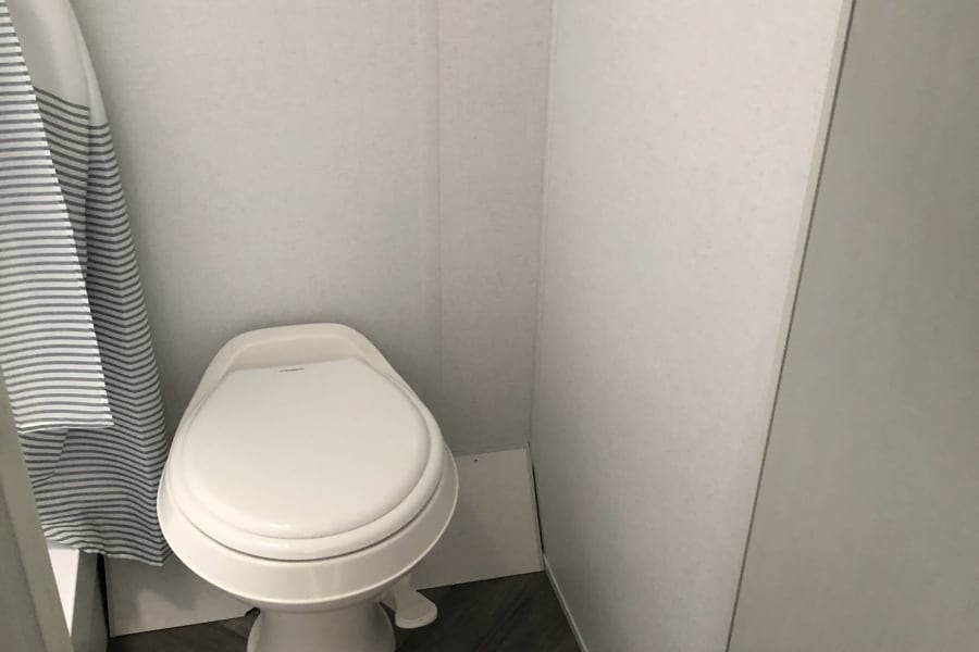RV rental bathroom: compact toilet, striped shower curtain, & rolled towels, perfect for your travels.