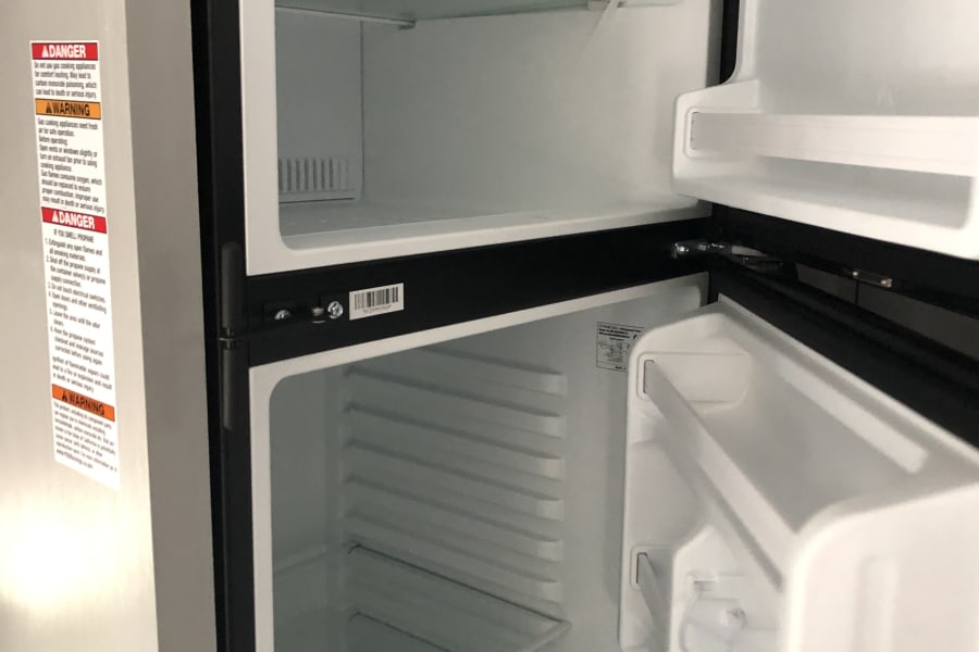 An open, empty refrigerator in an RV rental, revealing clean shelves and door storage. Ready for your trip!