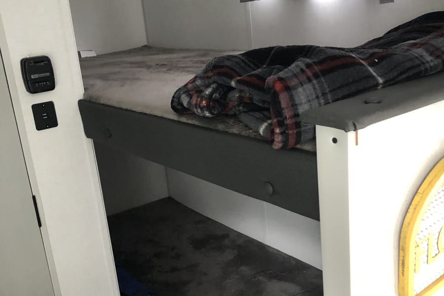 RV rental: Bright interior with cozy bunk beds. The top bunk has a plaid blanket, the bottom for bedding and a blue bag.