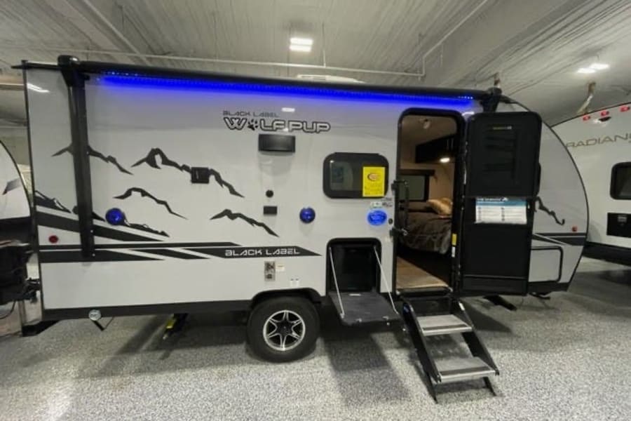 This Black Label Wolf Pup travel trailer, with mountain graphics and blue awning light, is perfect for your rv rental adventure.