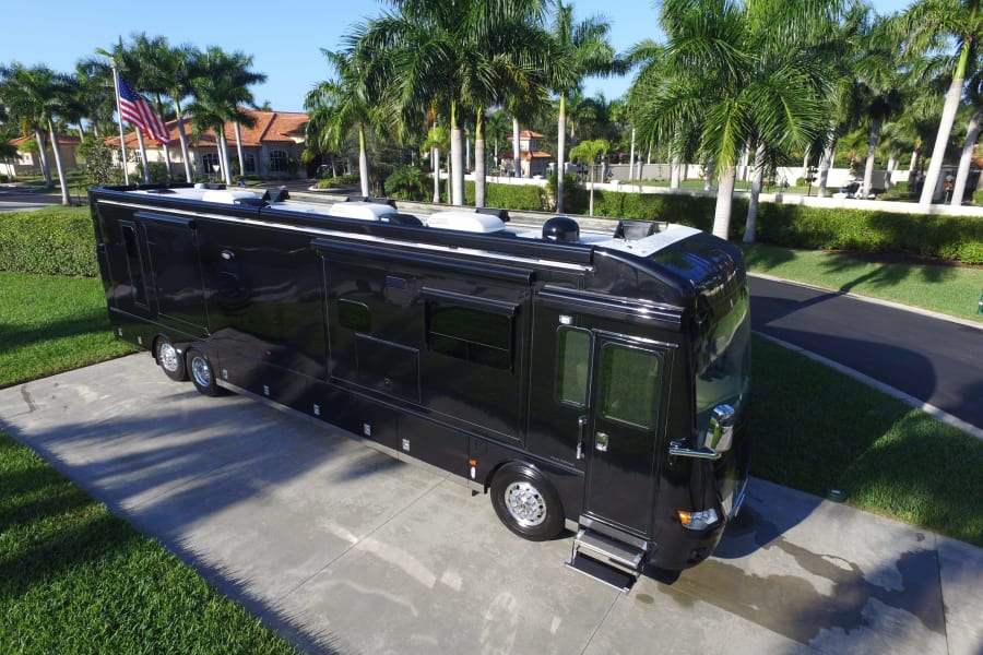 Luxury black motorcoach parked on a sunny driveway, surrounded by palm trees. Ideal for an rv rental.