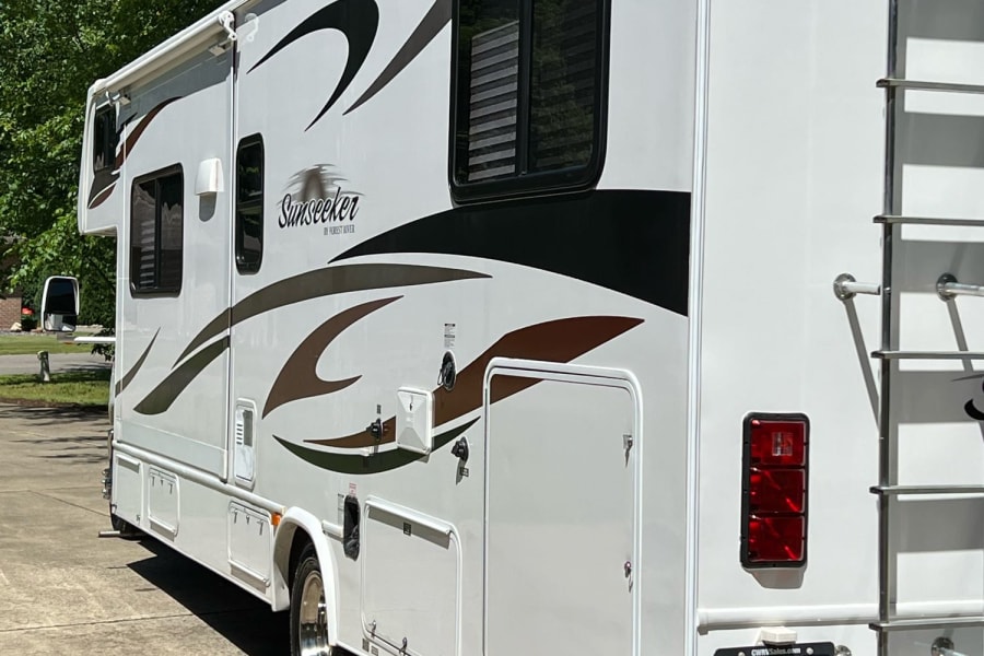 White Forest River Sunseeker RV rental, a Class C motorhome, shown from the side/rear on a driveway.