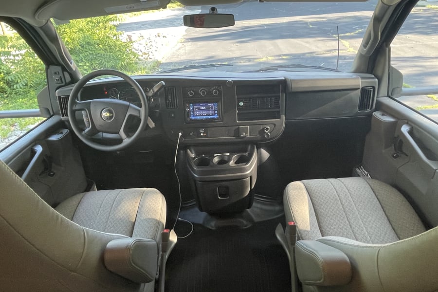 The spacious interior of a modern RV rental van, showing its dashboard, steering wheel, and front grey seats.