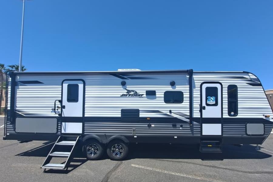 Modern grey & white travel trailer, ideal for RV rental. Steps extended for your next outdoor camping adventure.