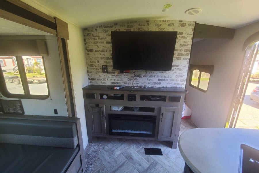 Modern RV rental interior: cozy living area with TV, faux brick wall, fireplace, and comfortable seating.