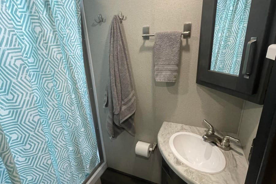This RV rental bathroom features a vibrant teal geometric shower curtain, a compact sink, and a mirrored cabinet.