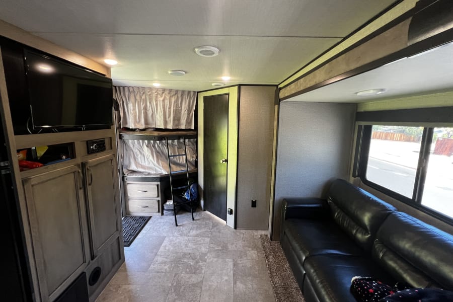 Cozy RV rental interior with bunk beds, a TV, comfortable sofa, and smart storage solutions for travel.