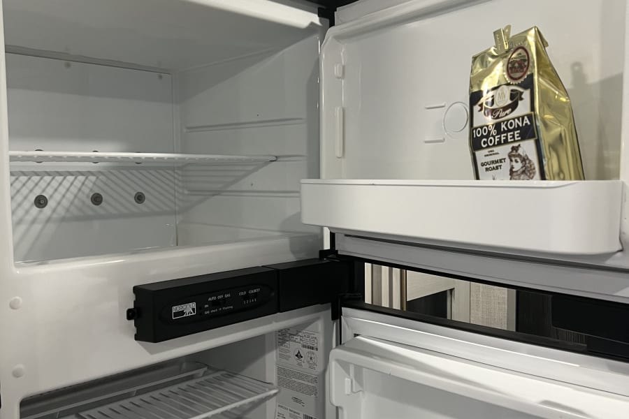 RV rental refrigerator open with a bag of 100% Kona Coffee inside, showing the Norcold controls and empty shelves.