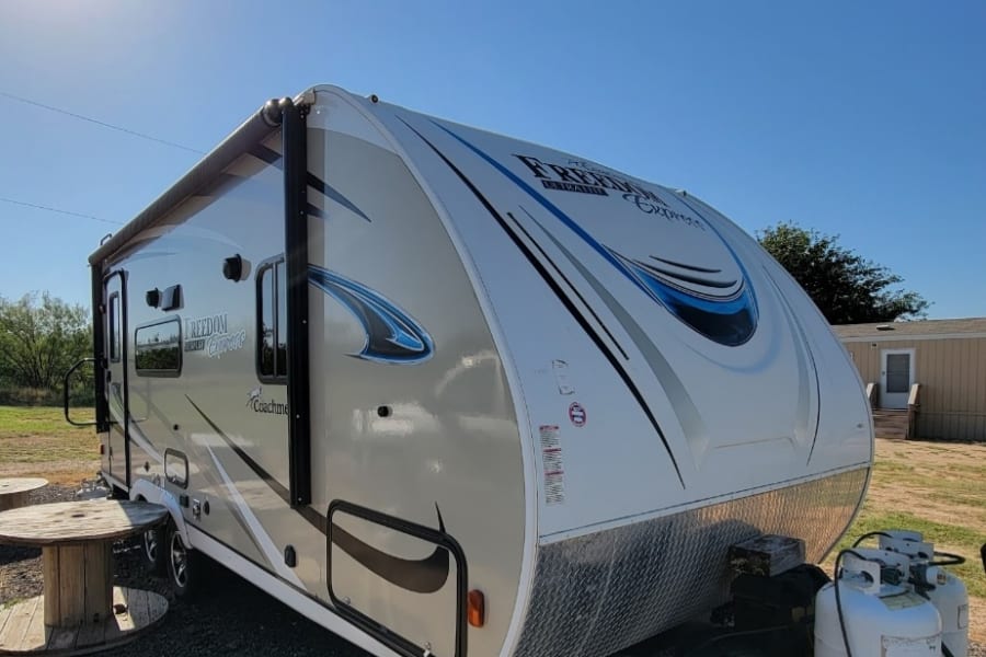 Under a clear blue sky, this sleek Coachmen Freedom Express RV rental travel trailer awaits your journey. Enjoy the outdoors!