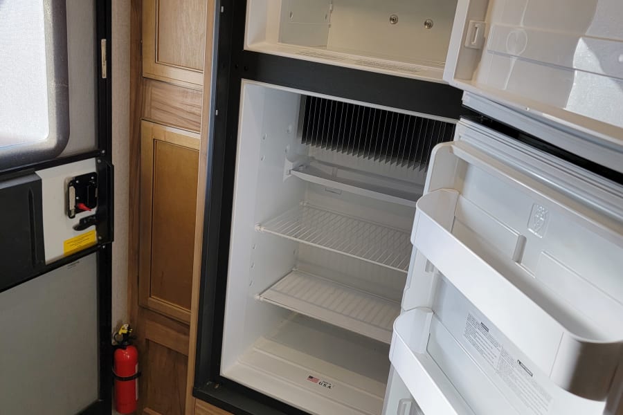 RV rental interior: Open refrigerator with fridge and freezer compartments. Shelves, controls, and a fire extinguisher are visible.