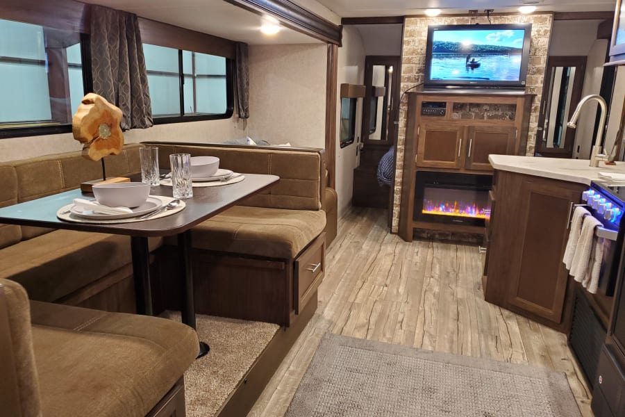 RV rental interior: dining booth, full kitchen, living area with TV & electric fireplace. Wood floors, modern and inviting.