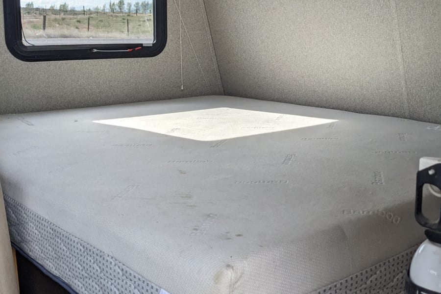 This RV rental features a comfortable bed with an Adventure mattress, window view, overhead storage, and a fire extinguisher.
