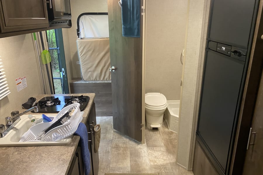 Inside an RV rental, showing the compact kitchen with sink, stove, microwave, a convertible bed, and a small bathroom.