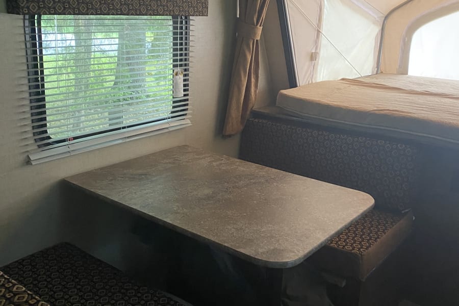Explore this comfortable RV rental interior: dinette, window, and pop-up camper bed area.