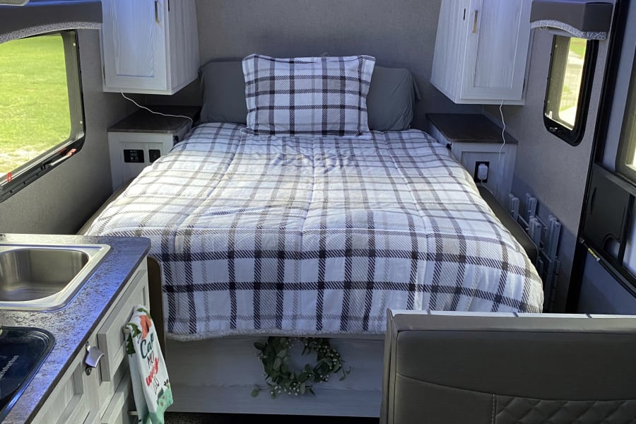 Cozy RV rental interior featuring a plaid bed, kitchen area, and dinette. Blue LED lights add ambiance.