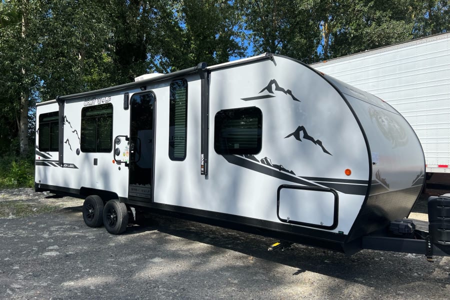 White Grey Wolf travel trailer RV rental, featuring mountain graphics and multiple windows, parked on gravel.