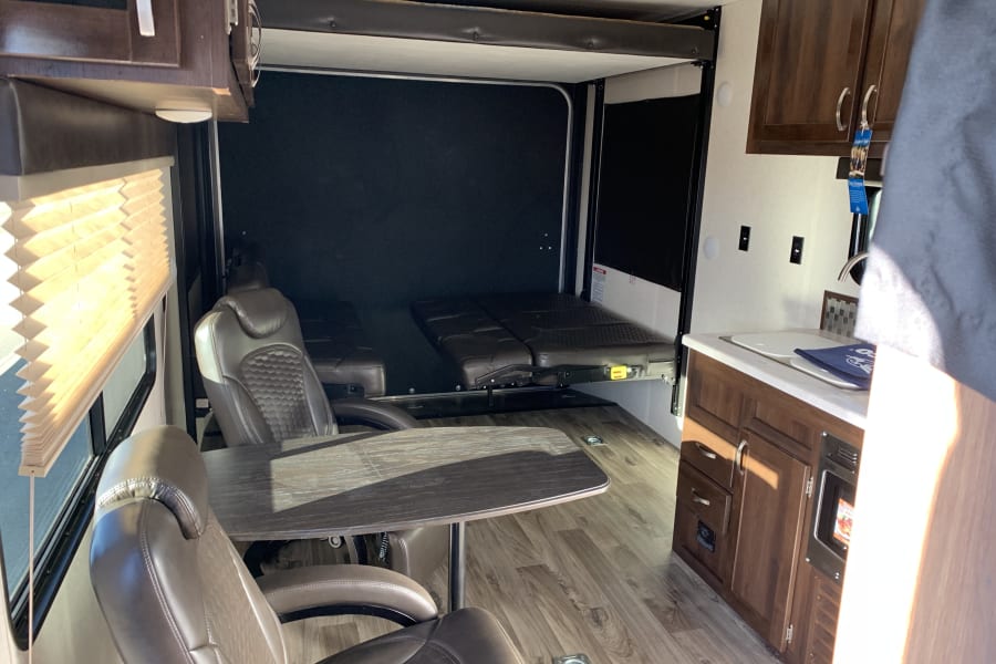 Bright RV rental interior: dining area, versatile rear with fold-down beds/seats, and a full kitchen. Ready for travel.