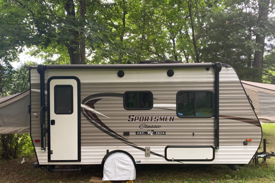This Sportsmen Classic hybrid RV rental is set up for camping in a wooded area, with its tent-like bunks extended.