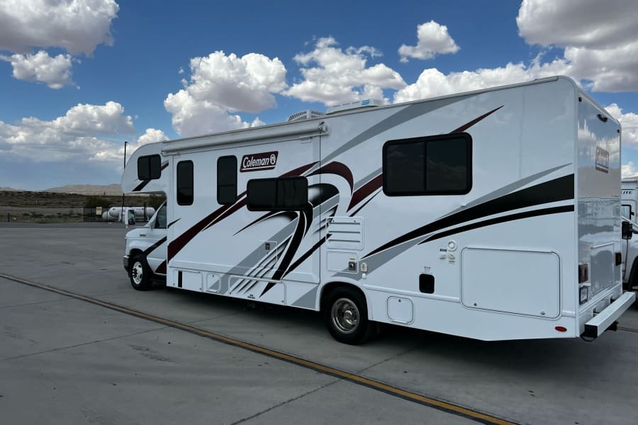 A white Coleman Class C RV rental parked under a bright blue sky with white clouds. Ready for your next adventure.