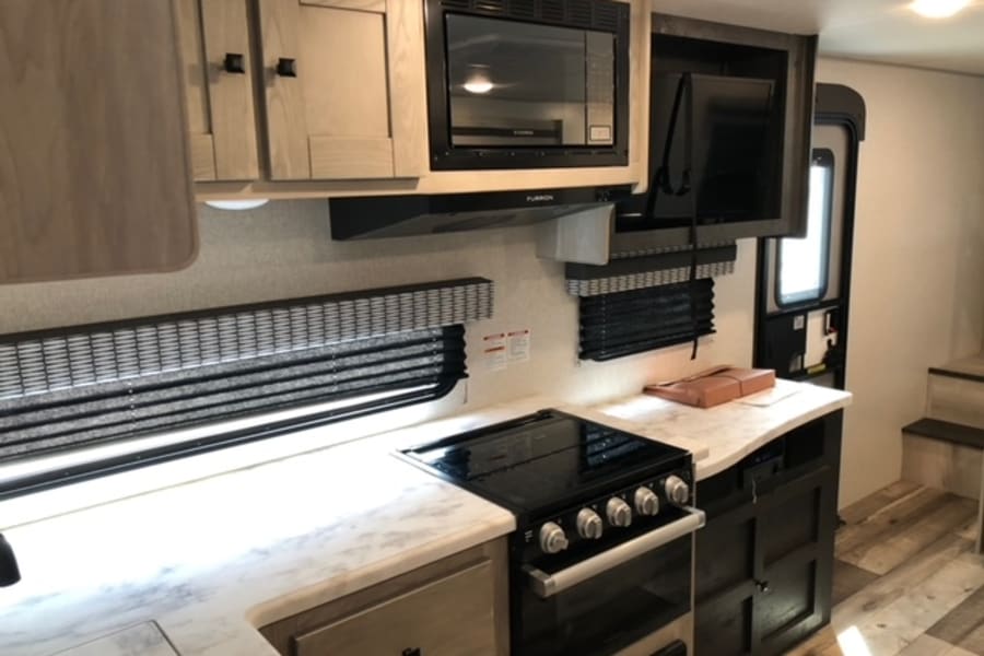 RV rental kitchen: Features black stove, microwave, light wood cabinets, spacious counter, and a large window.