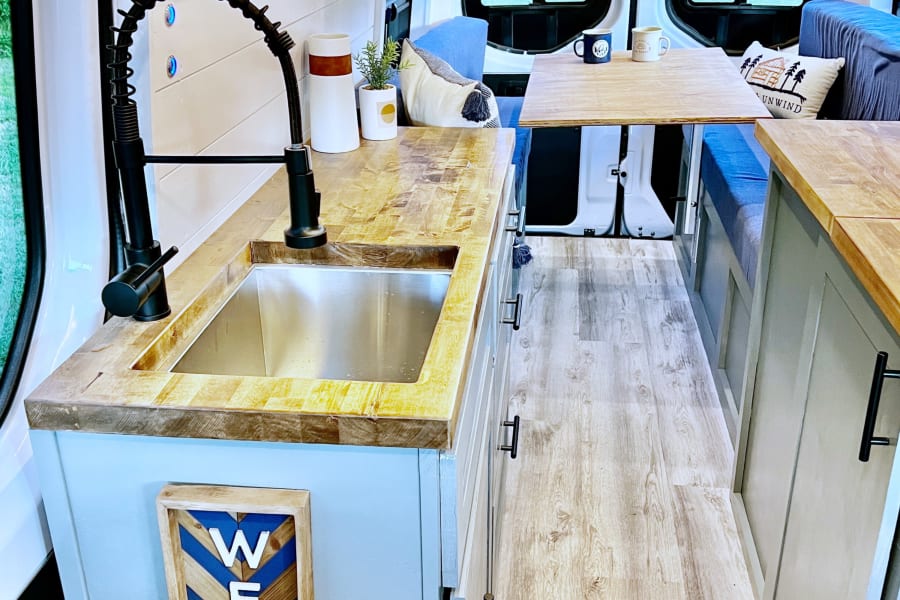 Bright and modern RV rental interior featuring a full kitchen with wood counters, a cozy dining space, and comfortable seating.