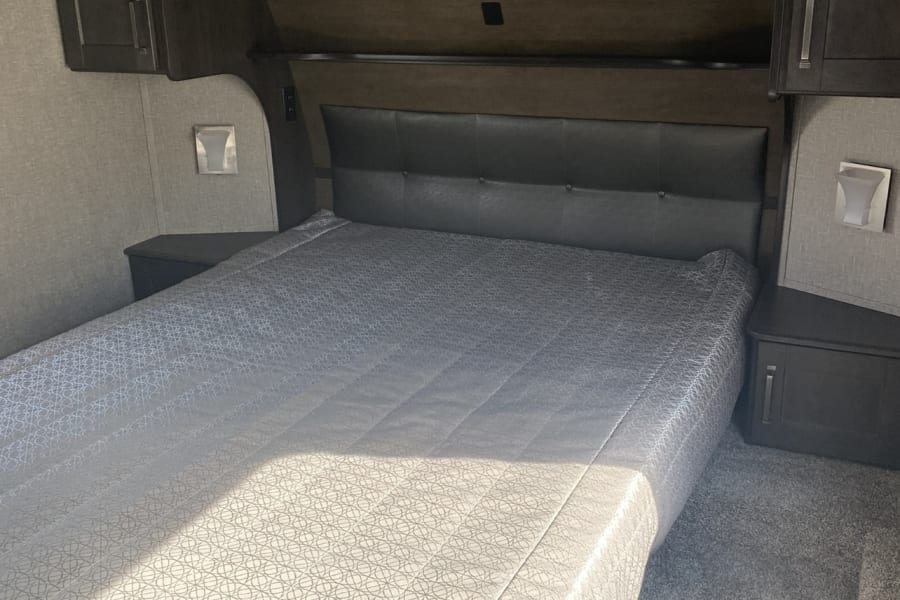 Cozy RV rental bedroom with dark cabinets, headboard, and patterned bed.