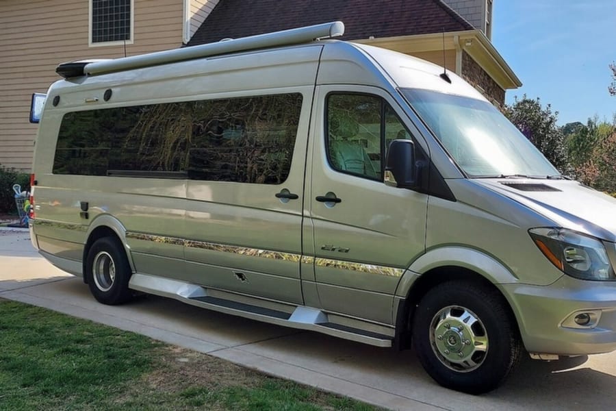 Full side view of a silver Mercedes-Benz Sprinter Class B RV, parked on a driveway, ready for an rv rental.