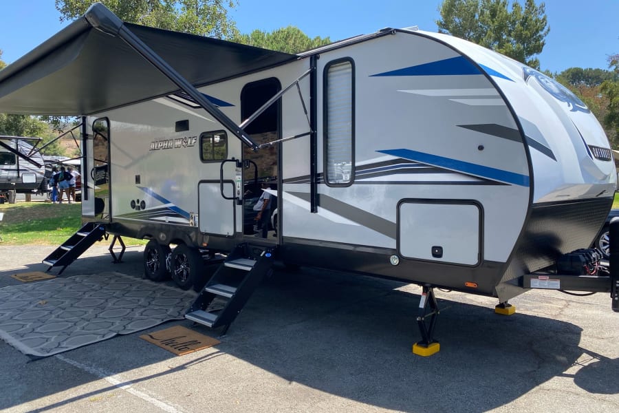 Spacious Alpha Wolf RV rental, featuring an extended awning, steps, and outdoor setup for a sunny adventure.