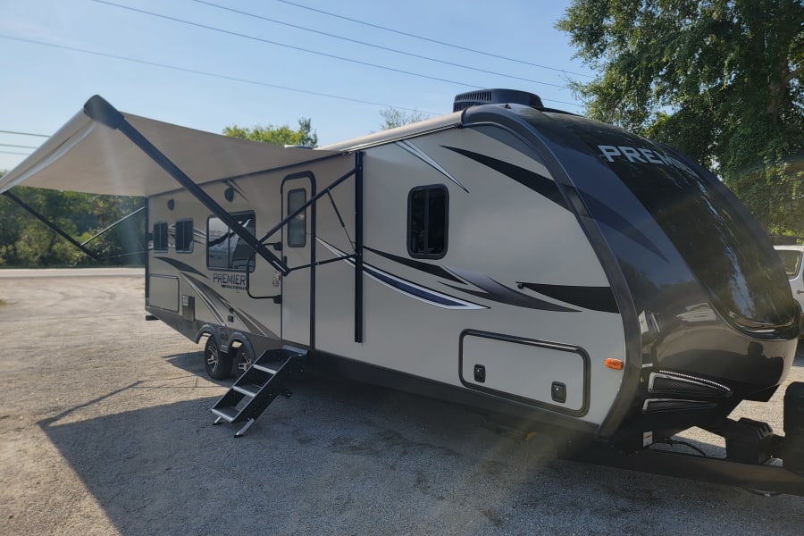 Spacious Premier travel trailer RV rental parked outdoors with awning extended and steps down.