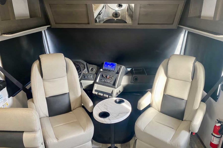 Spacious RV rental cockpit featuring comfortable driver & passenger seats, dashboard controls, and a marble-top table.