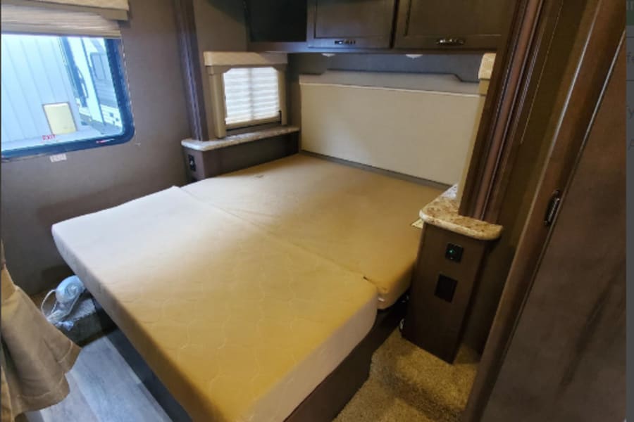Discover this cozy RV rental bedroom. Features a large bed, overhead cabinets, and steps, offering comfort for your travels.