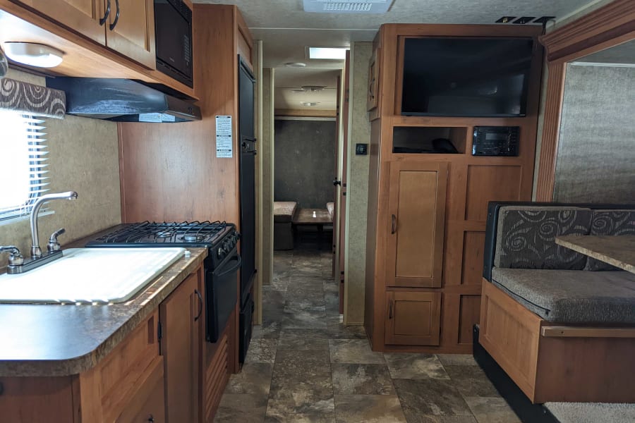 Spacious rv rental interior featuring a full kitchen with stove, microwave, and sink, plus a living area with TV and dining booth.