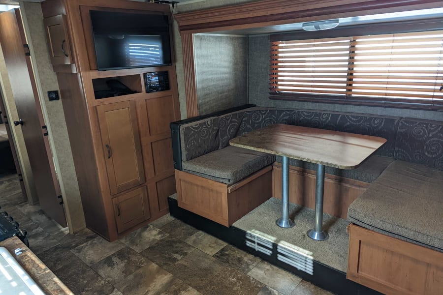 RV rental: View of a U-shaped dinette with patterned cushions, table, and entertainment center with TV. Wood cabinetry.