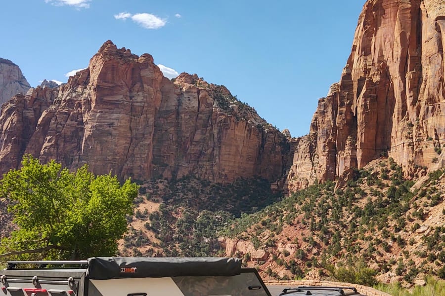 An RV rental: TETONX adventure trailer and Jeep on a road in a scenic red rock canyon under blue sky.