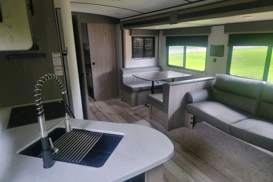 Modern RV rental interior: kitchen, dinette, and living area with a comfy couch.