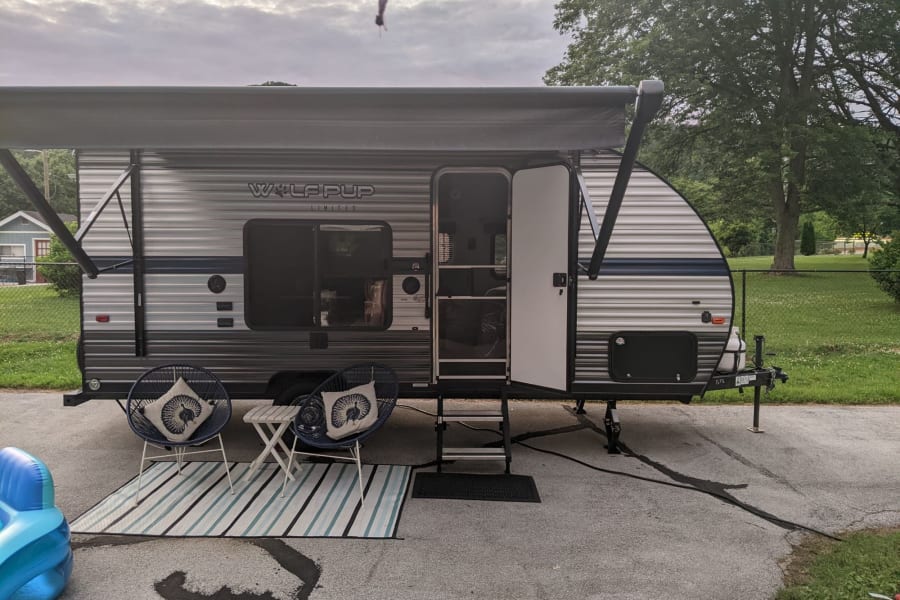 Relaxing RV rental patio with awning, outdoor seating, and rug for comfortable camping. Perfect for travel trailer adventures.