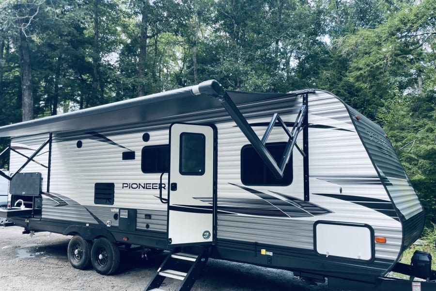 This Pioneer rv rental is set up in a wooded campground with its awning out and steps down, ready for adventure.