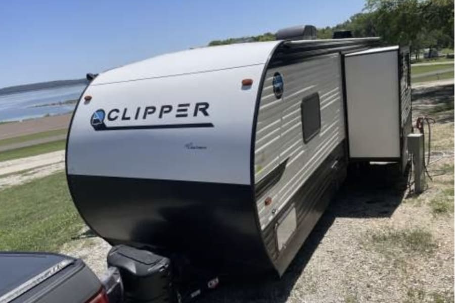 This Clipper travel trailer RV rental is parked lakeside, ready for a sunny camping trip and outdoor adventures.