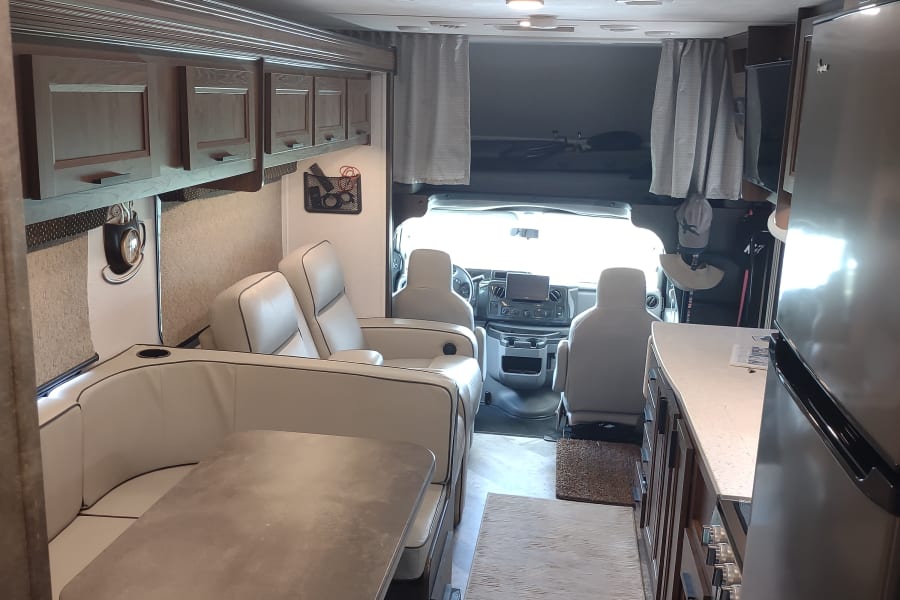Bright, modern RV rental interior featuring a lounge/dining area, kitchen counter, and cockpit view. Perfect for adventures.