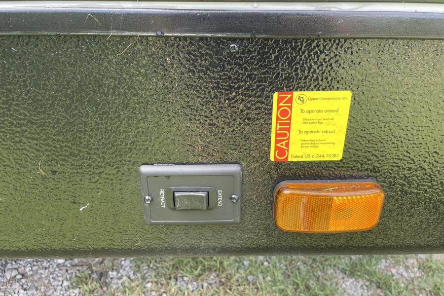 RV rental: Lippert leveling system control switch (extend/retract), safety sticker, and amber reflector.