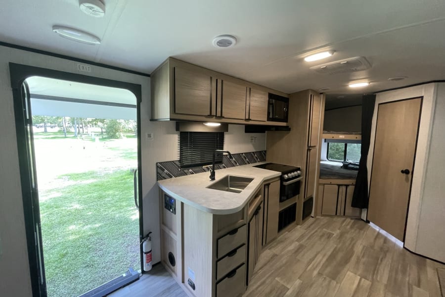 Modern RV rental interior with full kitchen, sink, stove, and bright open exit. Ready for your adventure.