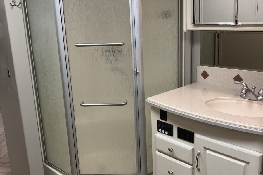 This RV rental bathroom features a glass corner shower, a vanity with sink, and an overhead mirror.