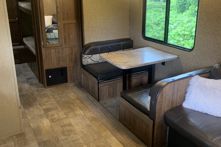 Interior of an RV rental featuring a dinette with bench seating, bunk beds, and a kitchen area. Bright, functional space.