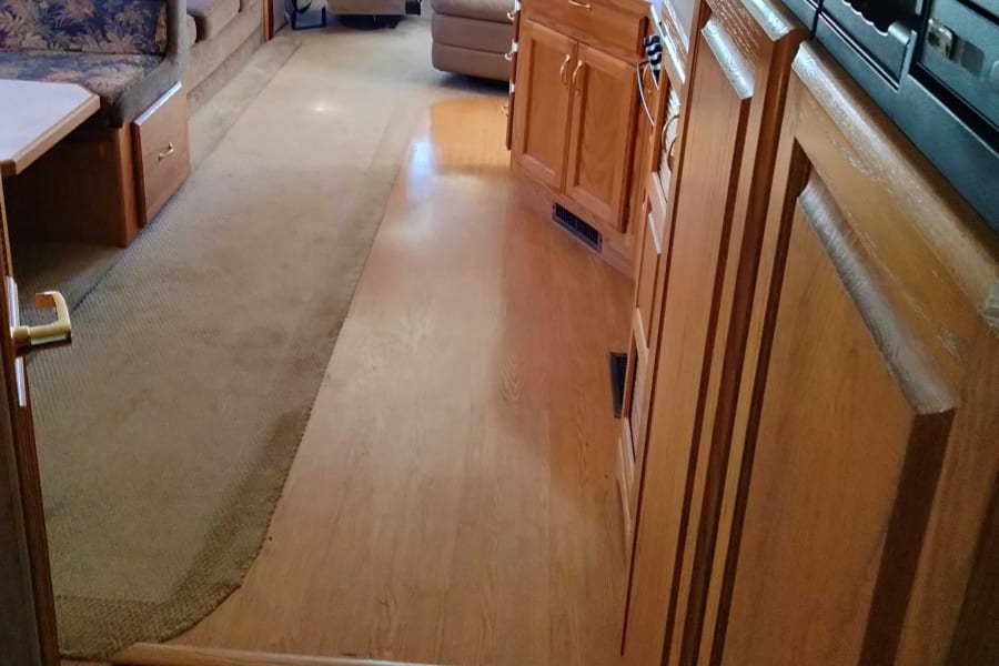 Spacious RV rental interior featuring a kitchen area with wood floors, and a living/dining space with carpeting and comfortable seating.